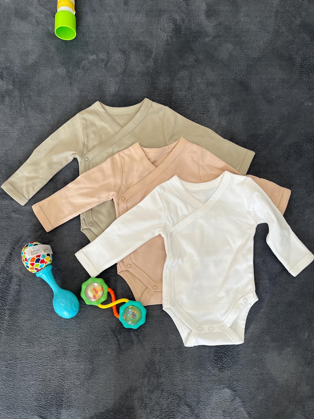 Three kimono rompers, green, brown and white, laid flat with a rattle and a pacifier